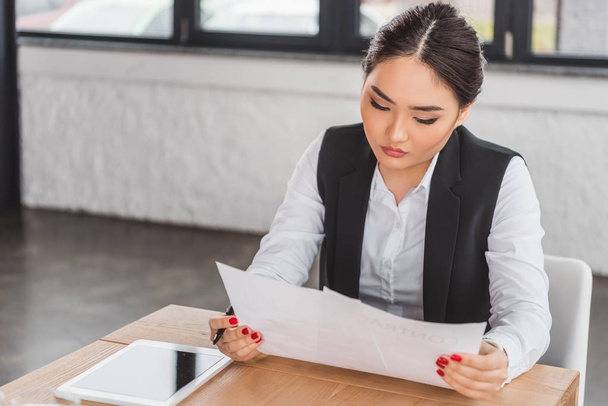 концентрированная молодая азиатская предпринимательница, имеющая документы и работающая в офисе
 - Фото, изображение