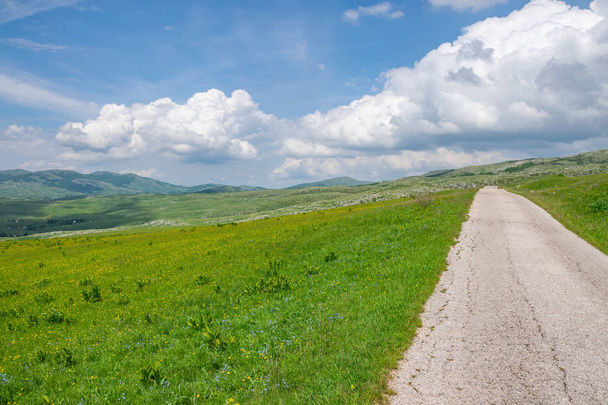 estrada estreita sinuosa leva através de prados pitorescos e montanhas
 - Foto, Imagem