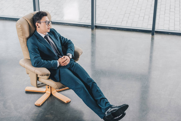 Blick aus der Vogelperspektive auf einen jungen Geschäftsmann im Anzug, der am Arbeitsplatz im Stuhl sitzt  - Foto, Bild