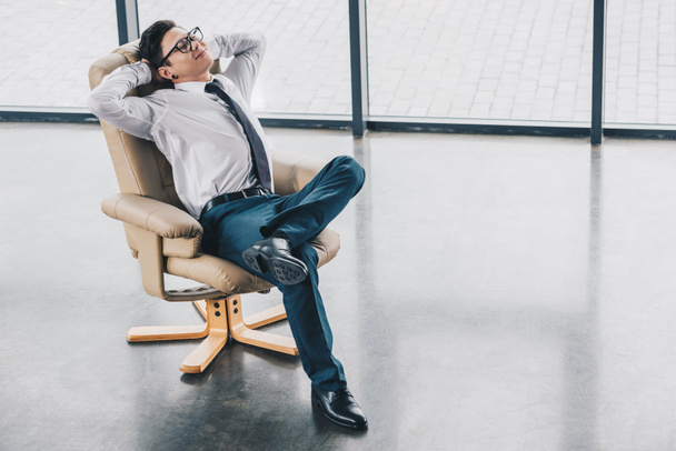 wysoki kąt widzenia młody biznesmen kazachski w okularach odpoczynku w fotelu w miejscu pracy - Zdjęcie, obraz
