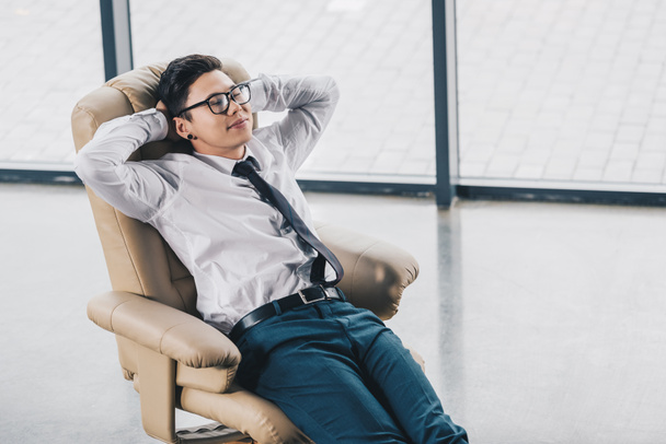 椅子で休んでいる眼鏡の若いアジア系のビジネスマンのハイアングル  - 写真・画像