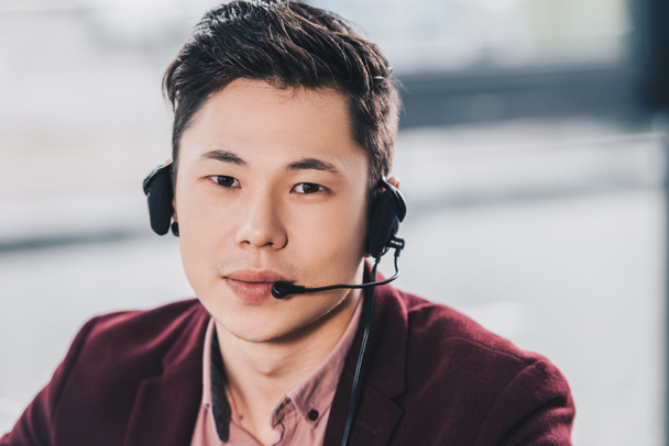 handsome young asian manager in headset looking at camera in office  - Foto, Imagen
