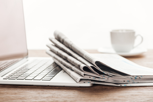 ノート パソコン、コーヒー カップと木製のテーブルの上の新聞のスタック - 写真・画像