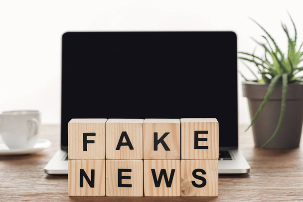 Holzwürfel mit Wörtern Fake News auf Laptop mit leerem Bildschirm auf Holztischplatte - Foto, Bild