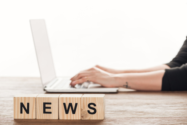 bijgesneden afbeelding van journalist werken bij laptop, houten blokjes met woord nieuws op tafelblad - Foto, afbeelding