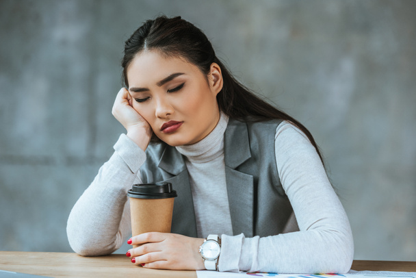 cansada joven empresaria sosteniendo café para ir y sentarse con los ojos cerrados en el lugar de trabajo
 - Foto, imagen