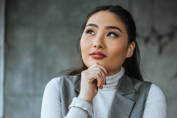 pensoso giovani asiatico donna holding mano su mento e guardando su in ufficio
 - Foto, immagini