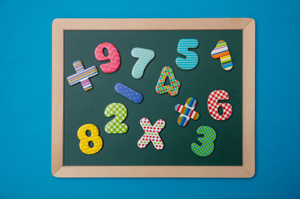 Mathematik, Schulkonzept. grüne Kreidetafel mit Holzrahmen, bunte Einsatzschilder und Zahlen, blauer Hintergrund - Foto, Bild