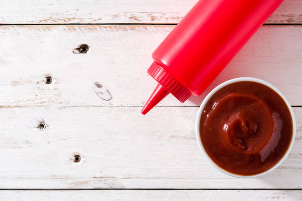 Ketchup-Sauce in Schüssel und Tomaten auf weißem Holztisch. Ansicht von oben. Kopierraum - Foto, Bild
