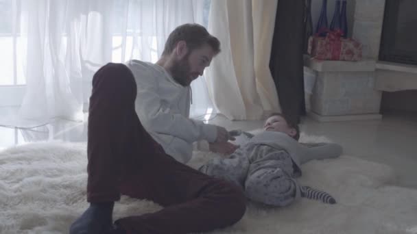 Bearded father talks with the child. Bearded dad and his son lying on the white carpet. Father agrees with the child. Father-child relationship. - Materiał filmowy, wideo