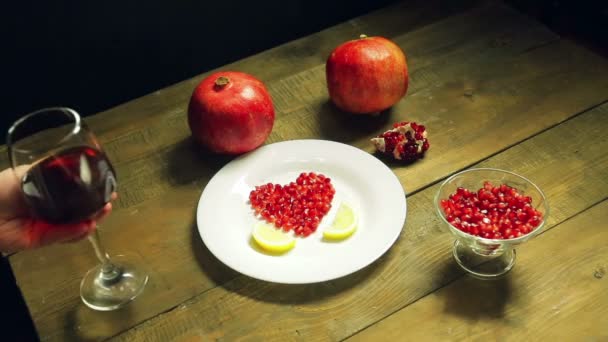 A woman puts on the table a glass of pomegranate juice. Fresh gragnates and a heart-shaped pomegranate dish are on the table. - Filmati, video