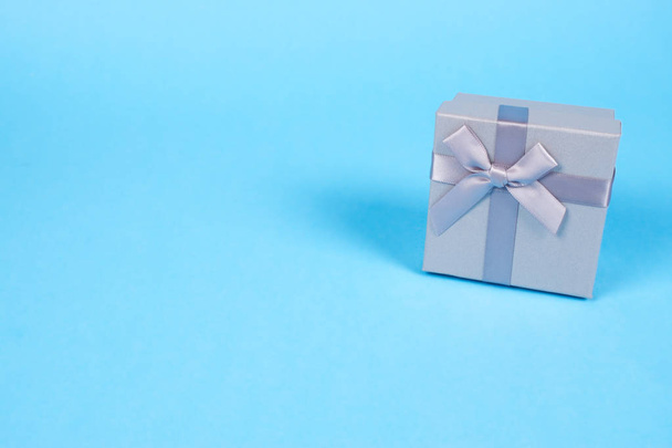 Belle boîte cadeau de couleur argent avec mignon petit arc en ruban soyeux sur fond bleu avec espace de copie. Concept de vacances
. - Photo, image