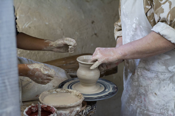 Een pottenbakker leert een kind hoe maak je een pot van klei. - Foto, afbeelding