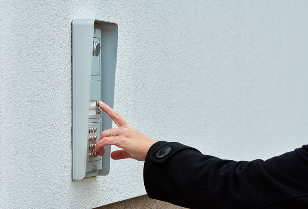 De vrouwelijke hand drukt op een knop deurbel met camera en intercom - Foto, afbeelding