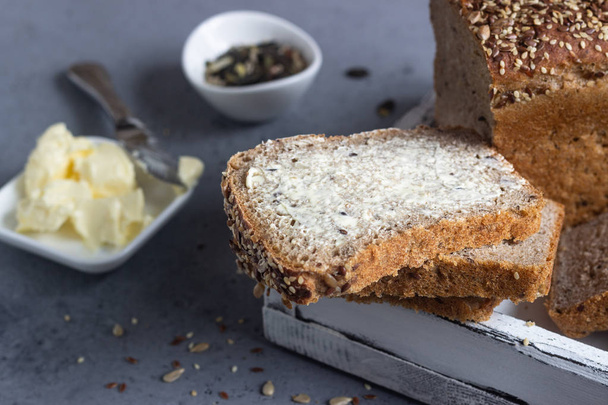 Sliced whole wheat bread baked with seeds and butter on wooden cutting board. Simple breakfast. - Zdjęcie, obraz