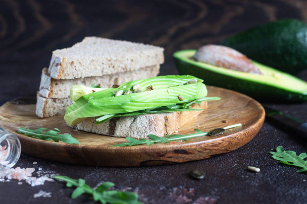 Healthy avocado sandwich for breakfast, lunch or snack with rye bread, sliced avocado, arugula and seeds. Diet and healthy food concept. - 写真・画像