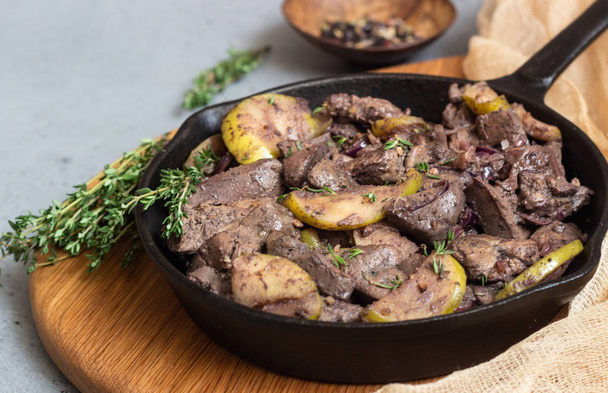 Fried chicken liver with apples, onions and thyme in a frying pan.  - Fotoğraf, Görsel