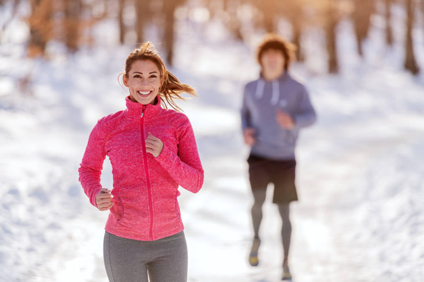 Dos amigos caucásicos deportistas felices calentándose antes de correr sobre la nieve. Invierno, concepto de estilo de vida saludable
. - Foto, imagen