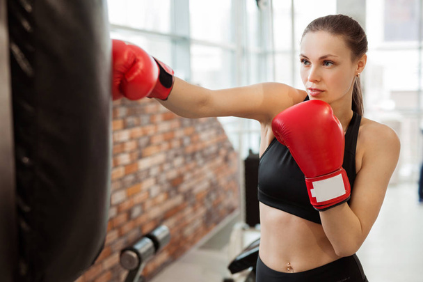 beautiful young girl in red boxing gloves is engaged in training in the gym - Foto, immagini