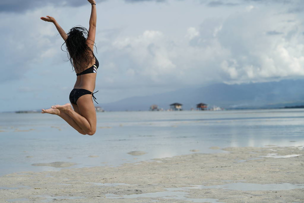 rear view of woman in bikini jumping on beach - Foto, Bild