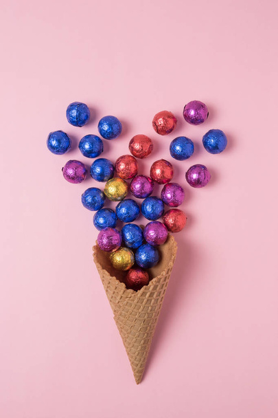 Ice cream cone with colored candyes on pink background. Minimal holiday concept. - Фото, зображення