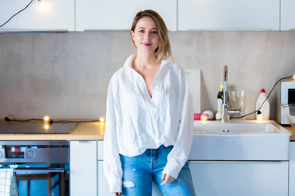 Young caucasian woman in white shirt and blue jeans stay on kitchen.  - Photo, Image