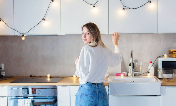 Giovane donna caucasica in camicia bianca e jeans blu soggiorno in cucina
.  - Foto, immagini