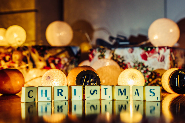 "Noel ahşap arka plan üzerinde harfler, Masa oyunu ile bulanık Noel ışıkları, meyve ve çikolata ile birlikte arka planda hediye Euro formunda" kelime. Uyum ve aile içinde sevgi kavramı - Fotoğraf, Görsel