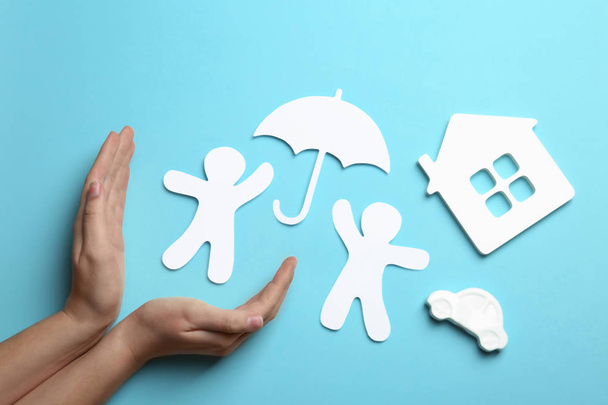 Woman holding hands near paper silhouettes of people with umbrella, car and house on color background, top view. Life insurance concept - Foto, imagen