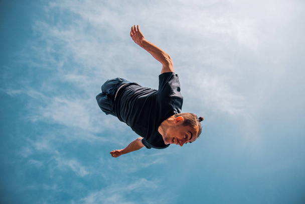 Young man practicing parkour exercise below blue sky - Photo, Image