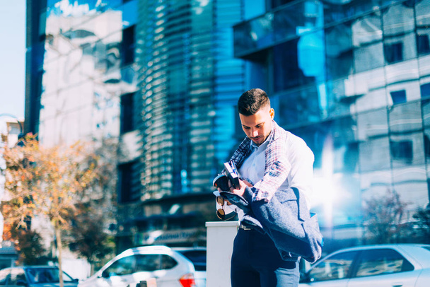 Joven hombre de negocios está caminando por el centro de la ciudad con su cuaderno y café en sus manos y mirando a su alrededor
 - Foto, Imagen
