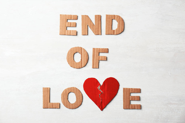 Phrase "End of love" with torn cardboard heart and letters on light background, top view. Relationship problems - Photo, Image