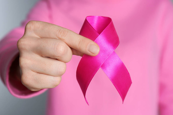 Woman holding pink ribbon on grey background, closeup. Breast cancer awareness - Zdjęcie, obraz