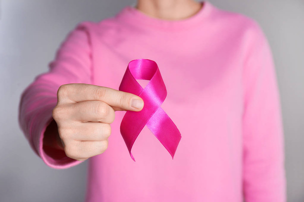 Woman holding pink ribbon on grey background, closeup. Breast cancer awareness - Foto, Imagen