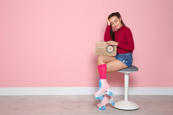 Young woman with roller skates and retro radio sitting on chair near color wall. Space for text - Foto, immagini