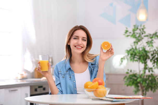 ジュース、台所のテーブルにオレンジ色のガラスと幸せな若い女。健康的な食事 - 写真・画像