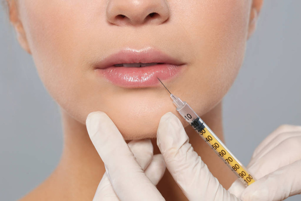 Jonge vrouw krijgen lippen injectie op witte achtergrond, close-up. Cosmetische chirurgie - Foto, afbeelding