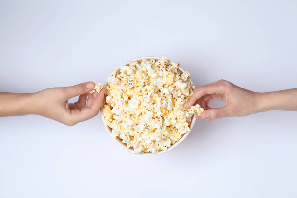 Women eating tasty popcorn from paper bucket on white background, top view - Zdjęcie, obraz