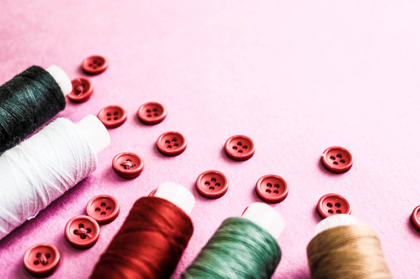 Beautiful texture with lots of round red buttons for sewing, needlework and skeins of spools of thread. Copy space. Flat lay. Pink, purple background - Photo, Image