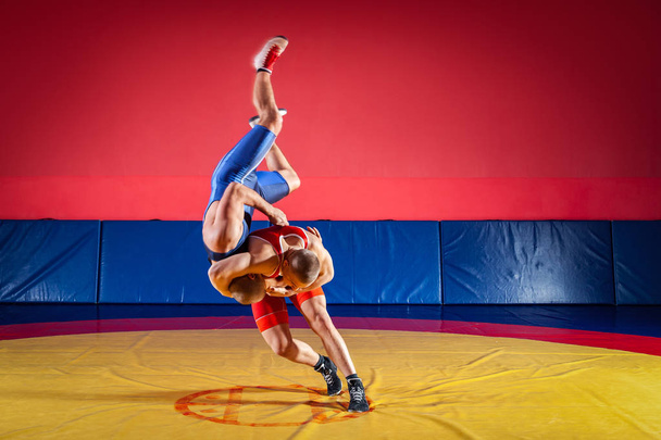 Koncept veletrhu wrestlingu. Dva mladíci v modré a červené zápas punčocháče jsou wrestlng a dělat suplex zápas na žlutém zápas koberec v tělocvičně - Fotografie, Obrázek