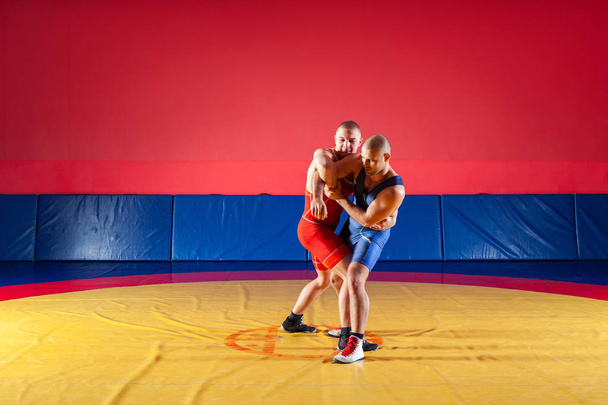 Deux lutteurs forts en collants de lutte bleus et rouges luttent et font une lutte suplex sur un tapis de lutte jaune dans la salle de gym. Jeune homme faisant grappin
. - Photo, image