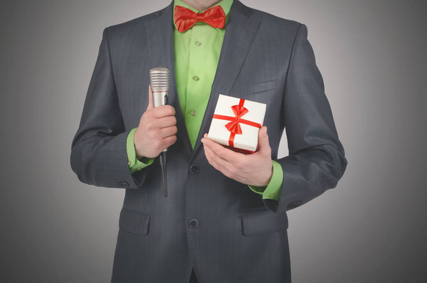 Gift box with a red bow and a radio microphone in a presenter hands on a gray background. - 写真・画像