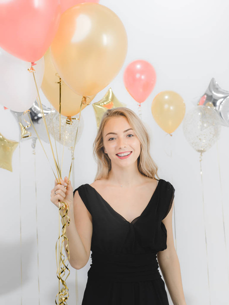 Όμορφη νεαρή γυναίκα Καυκάσιος σε μαύρο φόρεμα, ευτυχής χαμογελαστοί εκμετάλλευση πολύχρωμα μπαλόνια στο fun παρτυ, στούντιο κατακόρυφος βολή λευκό φόντο. - Φωτογραφία, εικόνα