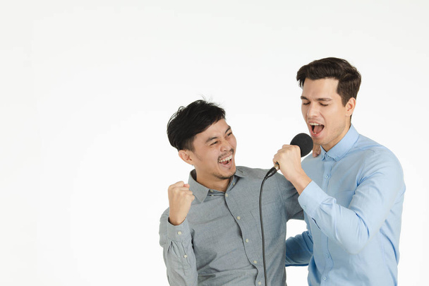 Half-length studio portrait of two young, handsome men, arms in arms, hold microphone, enjoy singing karaoke, celebrating some special occasion, standing on isolated white background - Fotó, kép