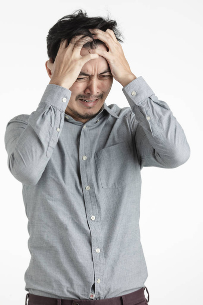 Half-length studio portrait of black hair, young Asian man in gray shirt, hands clenching his head,frowning, suffering from headache or stress, or upset on something on isolated white background - Photo, Image
