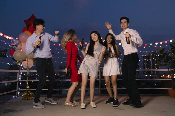 Группа фрейндов, азиатских и кавказских наслаждаться вместе в после рабочей партии на крыше здания. Светло-голубое небо города на заднем плане
 - Фото, изображение