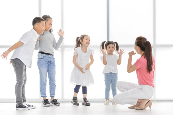 Ázsiai tanár nő rózsaszín ing tanítani ázsiai lányok és fiú néhány színész játszani hamis sírás, állnak előtt nagy fehér ablak. - Fotó, kép