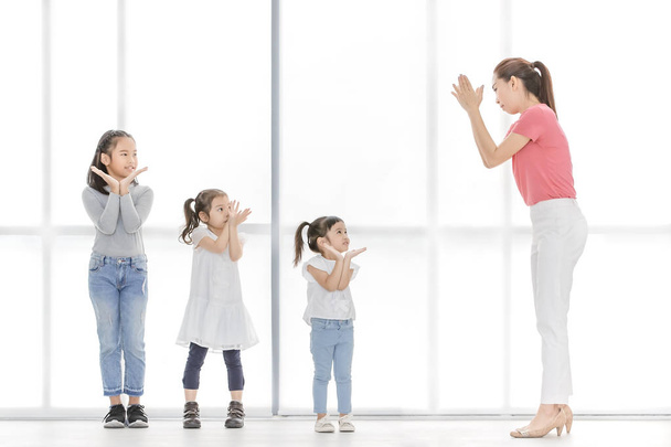 Mujer asiática con camisa rosa enseñan a los niños a jugar algo, se paran frente a una gran ventana blanca
. - Foto, imagen