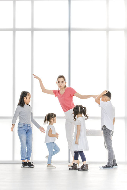 Ázsiai nő, rózsaszín póló tanítani ázsiai lányok és fiú csinál némely test mozgásának, hogy álljon a nagy fehér ablak. - Fotó, kép
