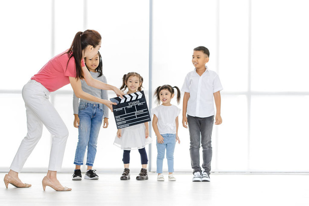 Asian woman in pink shirt Asian use clapper board in front of Asian boy and girls, they stand in front of big white window. - 写真・画像